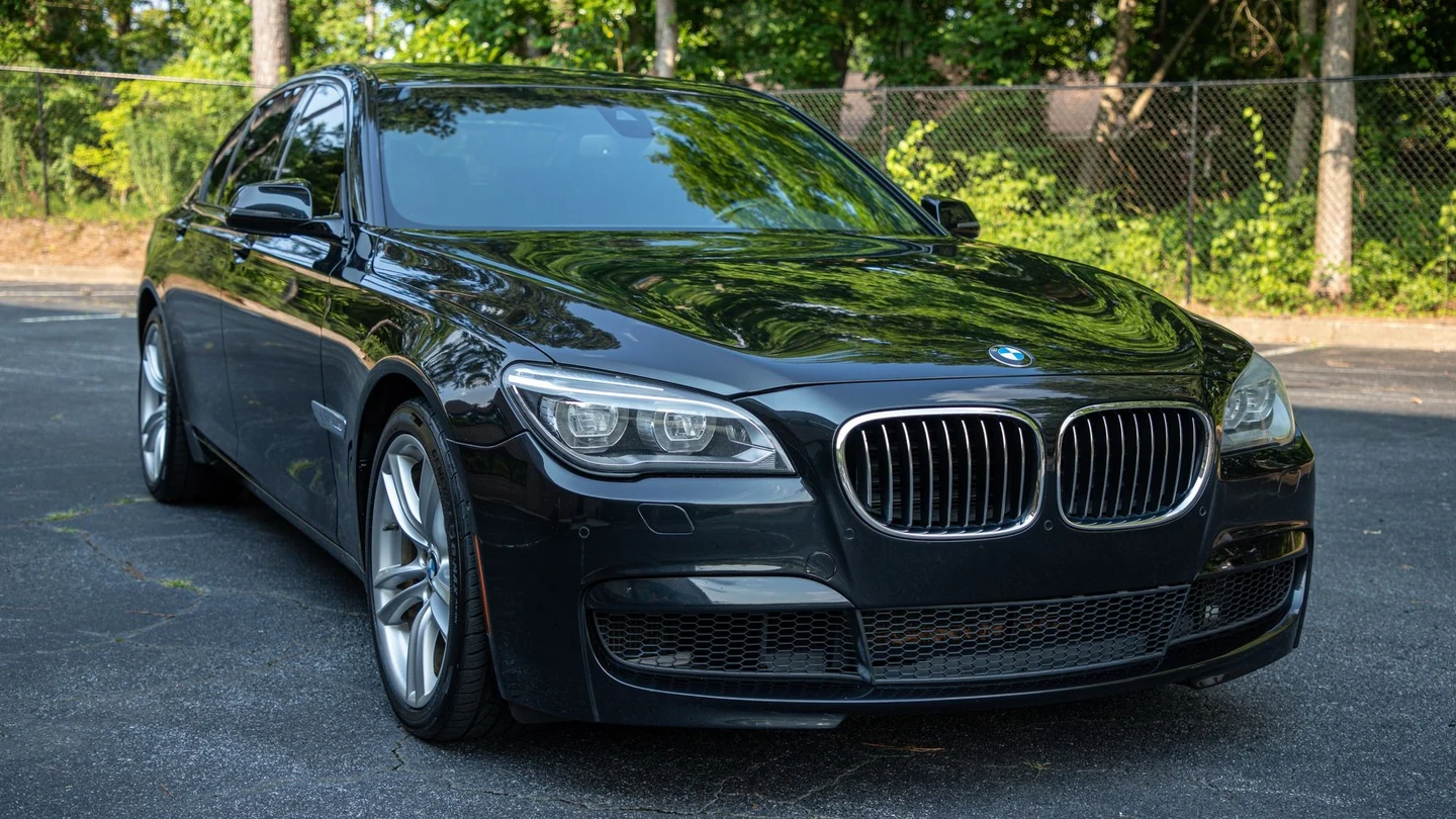 Glossy black BMW sedan in full front-three-quarter view, with crisp reflections across the hood