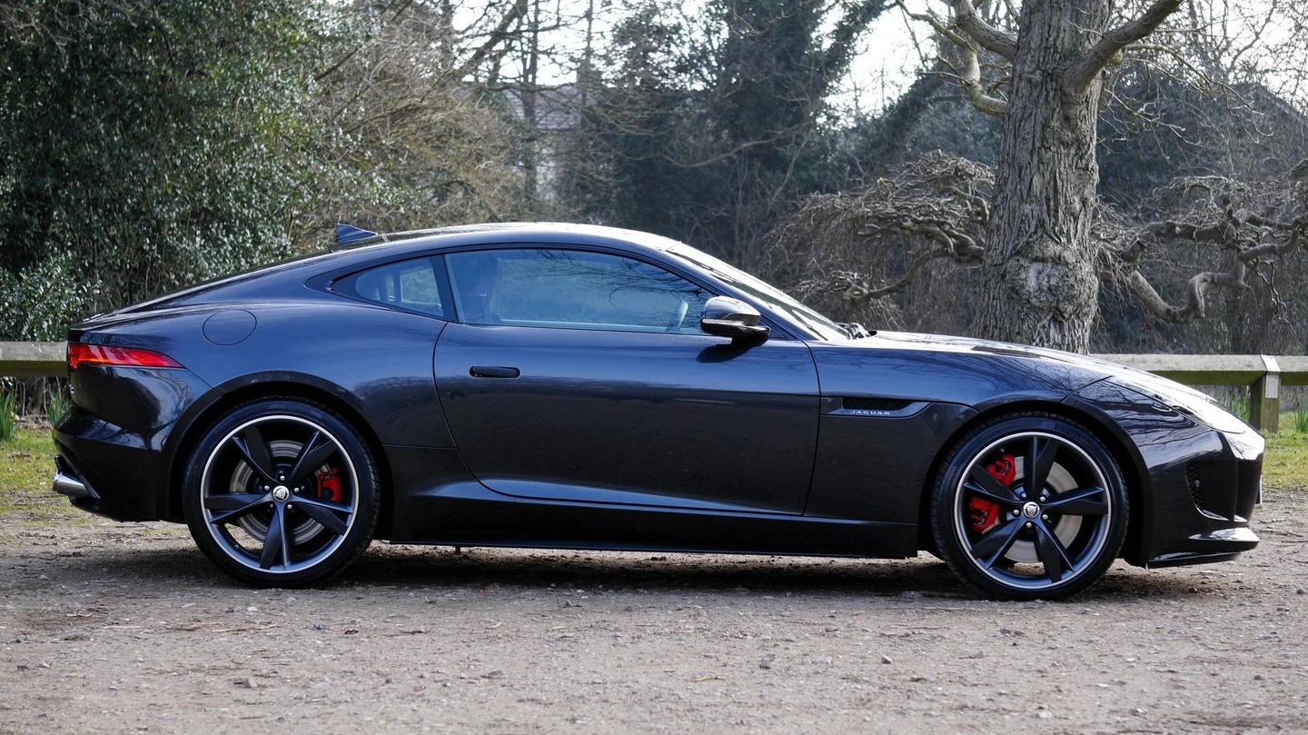 Dark Jaguar F-Type in full side profile, with reflective paintwork and red brake calipers