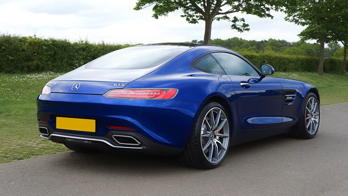 Glossy blue Mercedes-AMG GT in full rear-three-quarter view on a quiet country lane